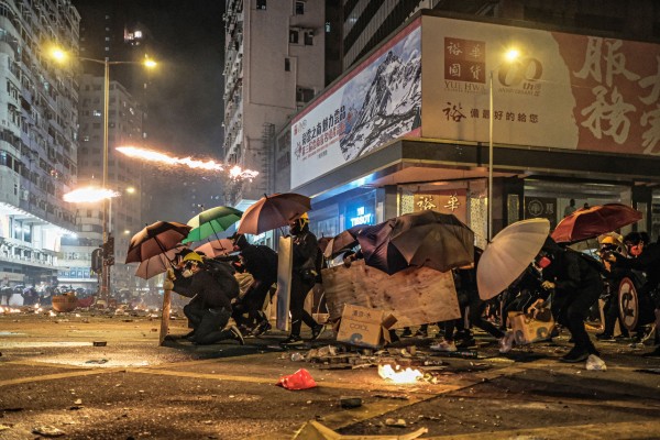 Protestierende mit Schutzausrüstung und Regenschirmen im Straßenkampf