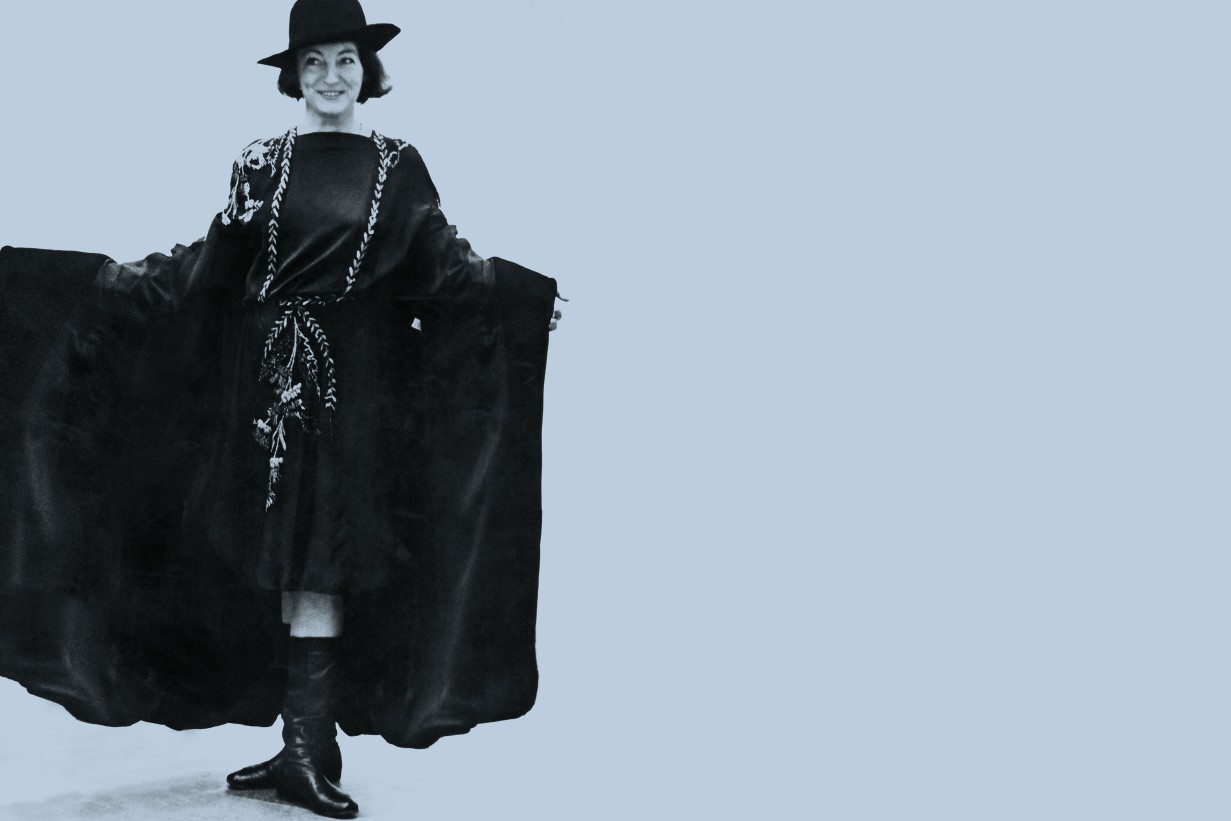 Schwarzweiß Fotografie: Darauf zu sehen ist eine weiße Frau in ein schwarzes Cape gehüült, sie lacht und trägt einen Hut.