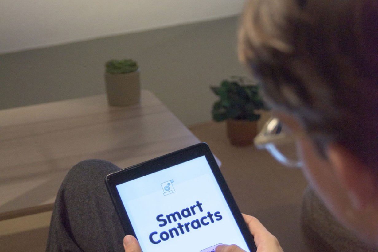 Eine Person hält ein Tablet, darauf zu lesen "Smart Contracts"