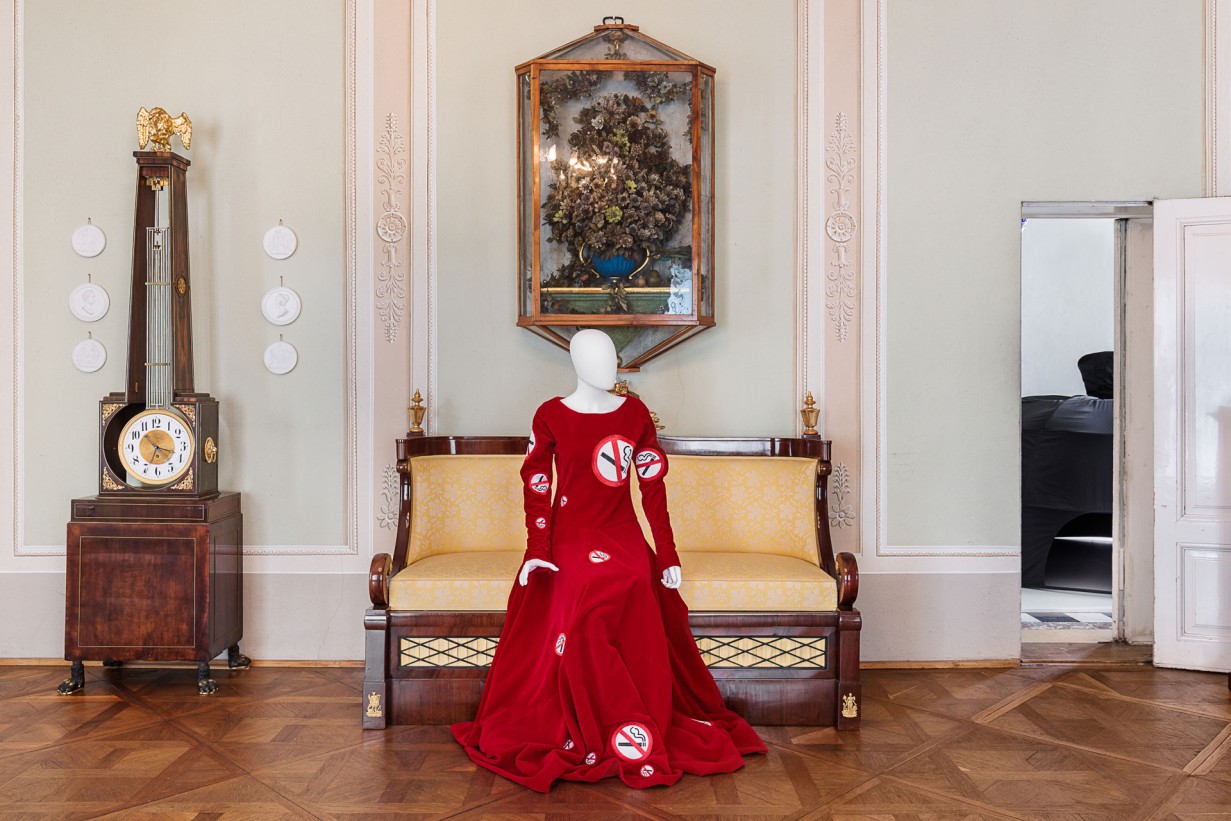 A mannequin sits on a canapé, she wears a red dress.