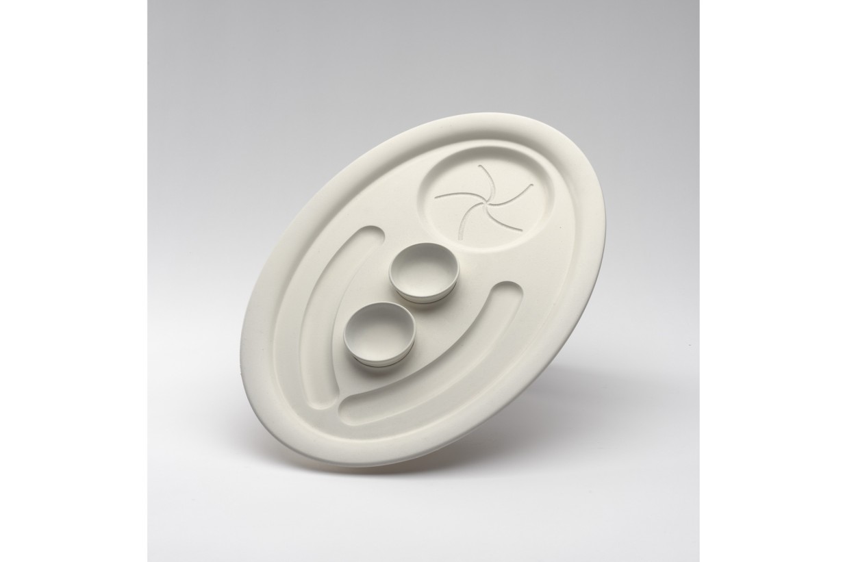 Ein weißer Teller mit Einbuchtungen für ein Paar Würstel, eine Semmel und zwei runden Ausbuchtungen in der Mitte