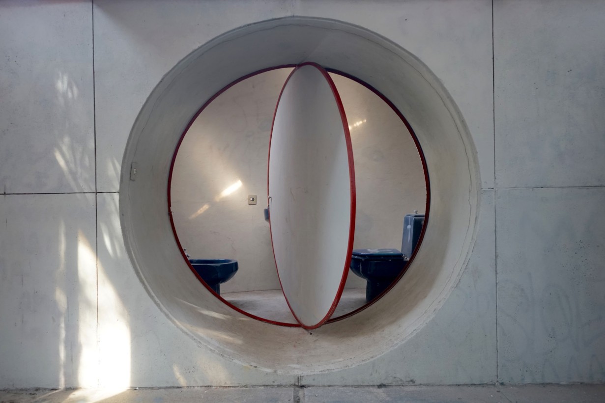 A concrete wall with a round opening, a room can be seen behind it