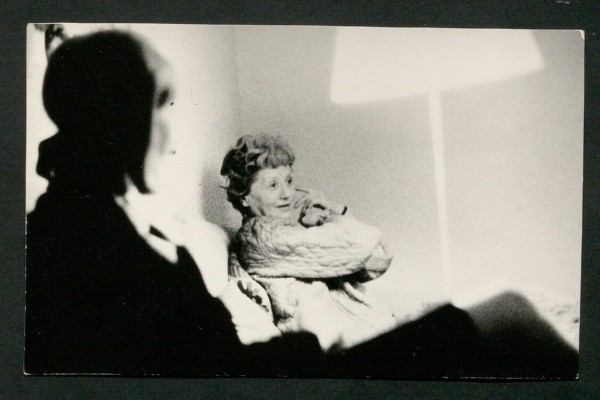 Black and white photograph, showing a blurred person in the foreground, a woman in the background