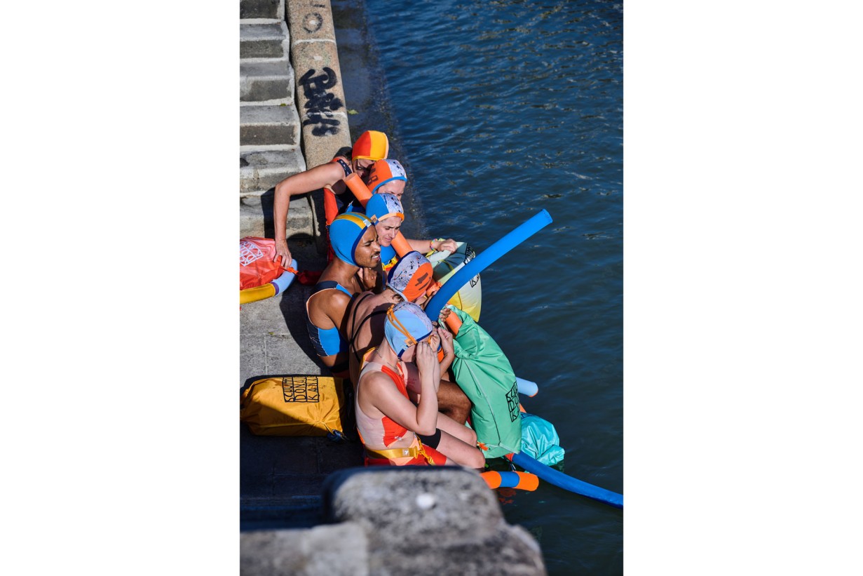 People in colorful swimwear sit by a canal
