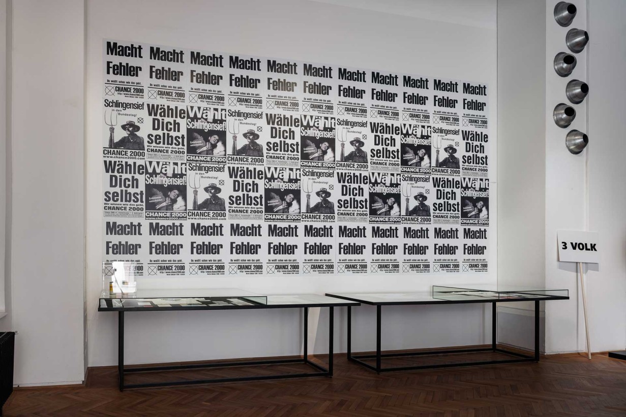 Plakatwand mit Slogans "Macht Fehler", "Wähle dich selbst", Wählt Schlingensief"
