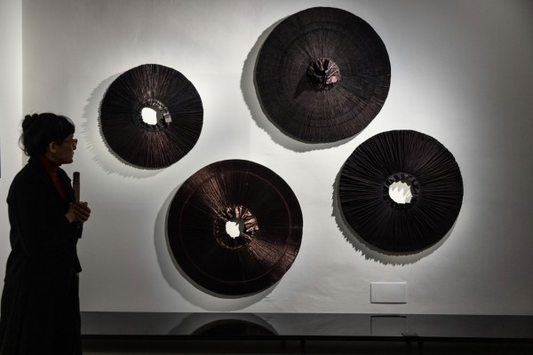 Four circular objects in dark colors on a white wall, the curator stands in front of them.