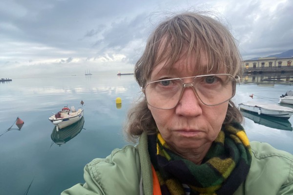 Portrait einer Frau, im Hintergrund Boote und Meer. 