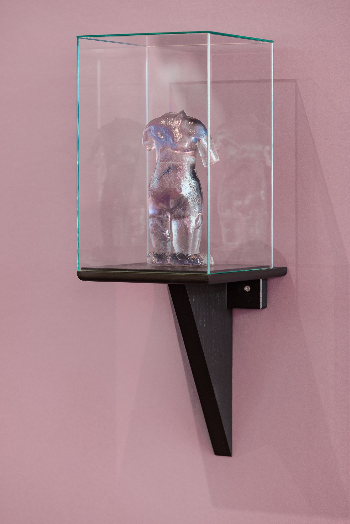 Exhibition hall, pale pink wall, on it a display cabinet with a transparent figure without a head containing a data chip
