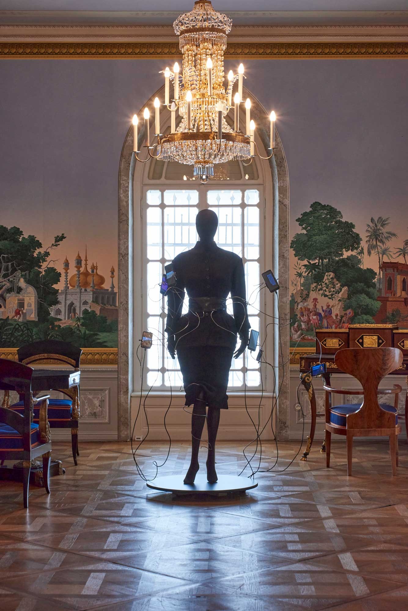 Ein Raum im biedermeierlichen Stil mit einer Schaufensterpuppe, die einen futuristischen Modeentwurf trägt. 