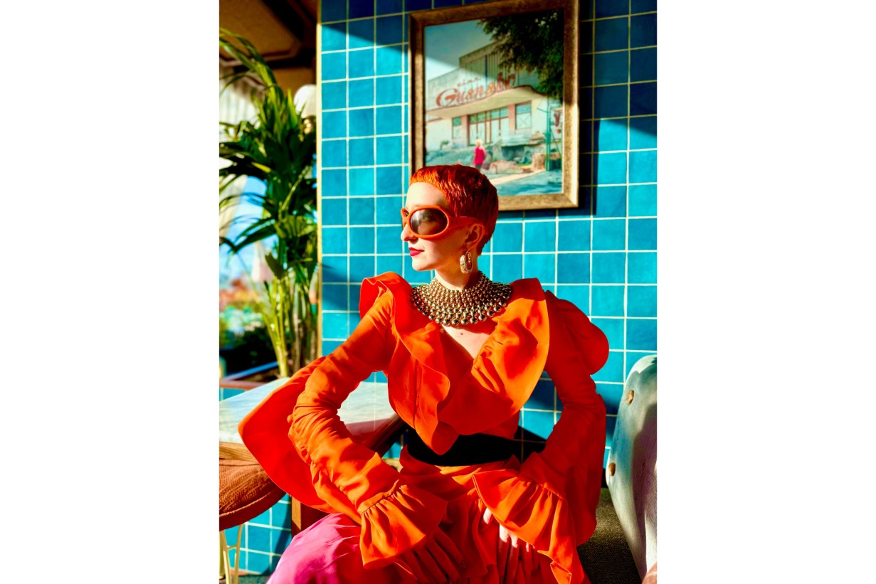 Judith Bradl in rot-orangem Kleid vor blau gefließter Wand