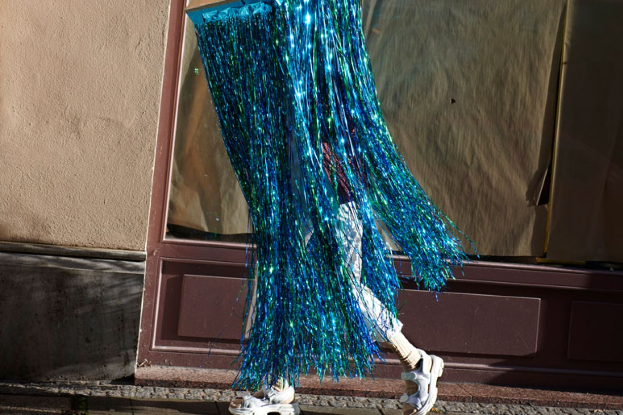 A blue skirt made of glitter raffia marches on white platform shoes on a sidewalk.