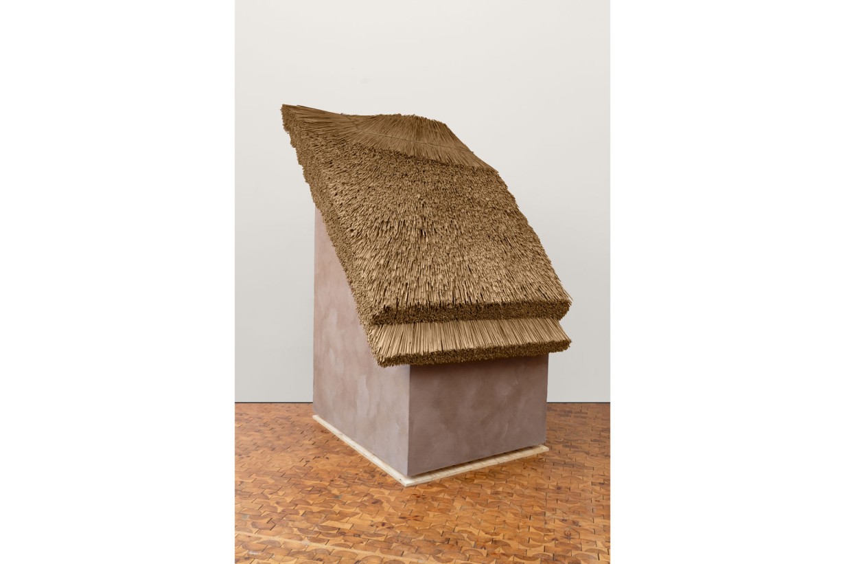 Ein kleines Haus mit Strohdach in einem Raum mit Parkettboden