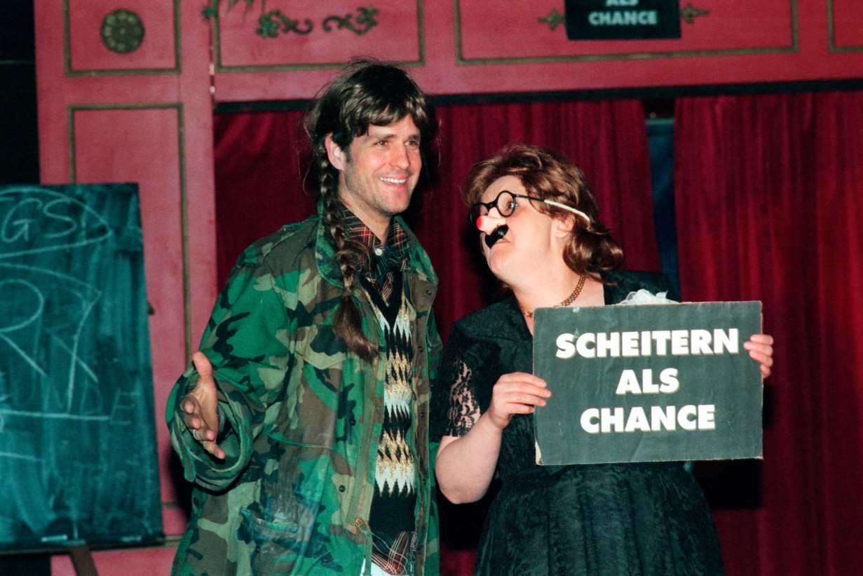 Christoph Schlingensief und Person die Schild hält "Scheitern als Chance"