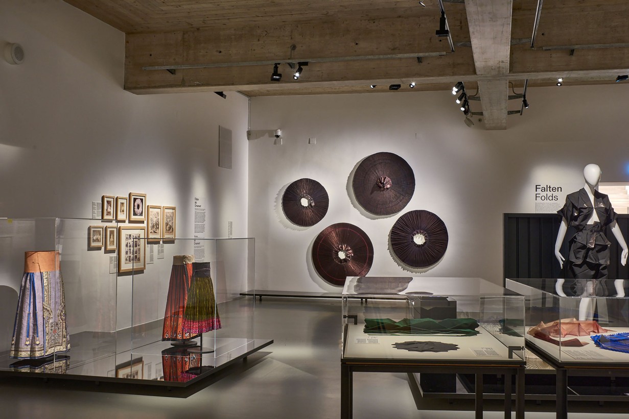 Exhibition space with objects: Pleated skirts, painting, photographs on the walls.