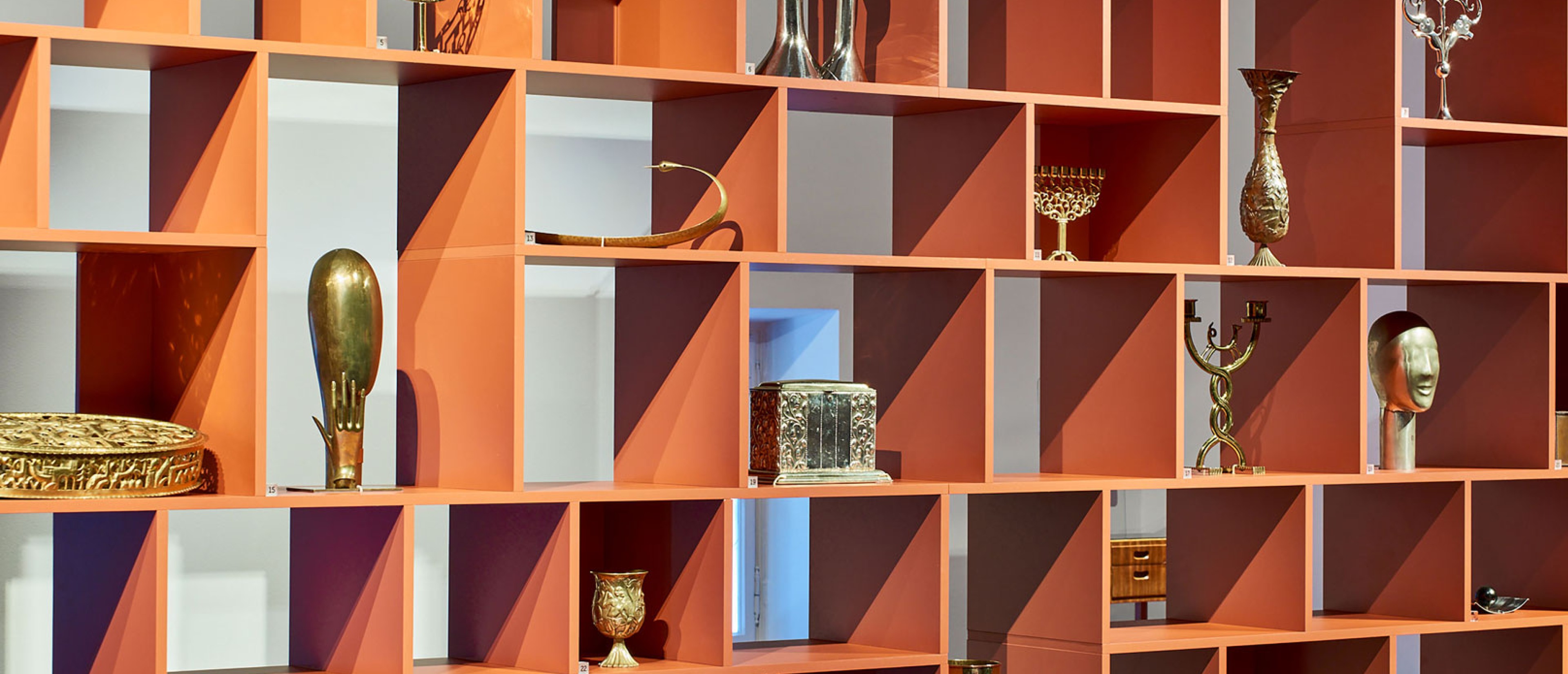 A shelf in oragne stands in the middle of a room and is filled with objects.