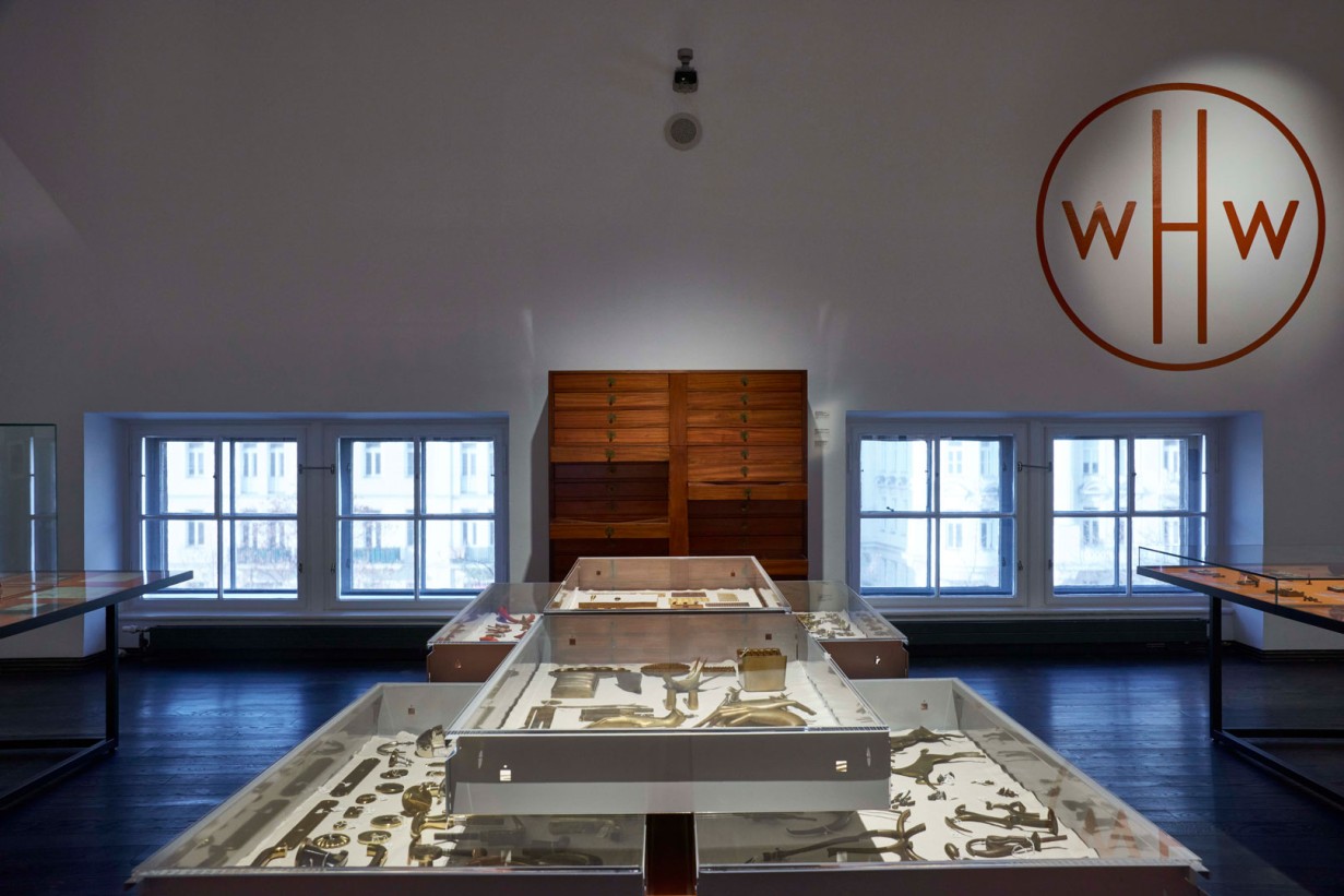 Ausstellungsraum mit Podest und Objekten, im Hintergrund steht WHW an der Wand