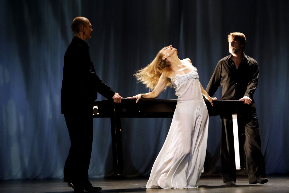 Two people in black on the left and right, with a dancer in a white dress in the center