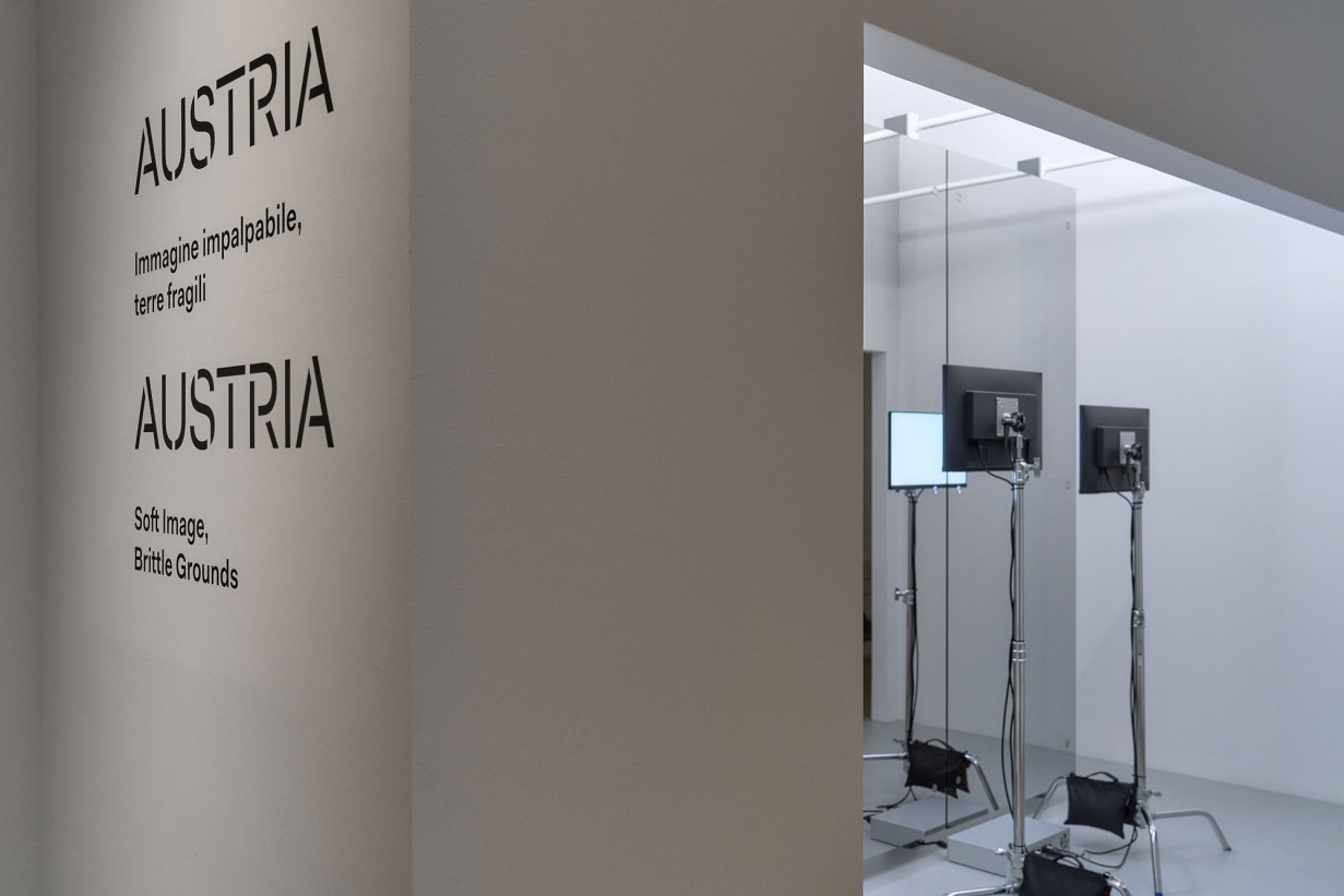 Exhibition space, text on wall “Austria”, screens in the background