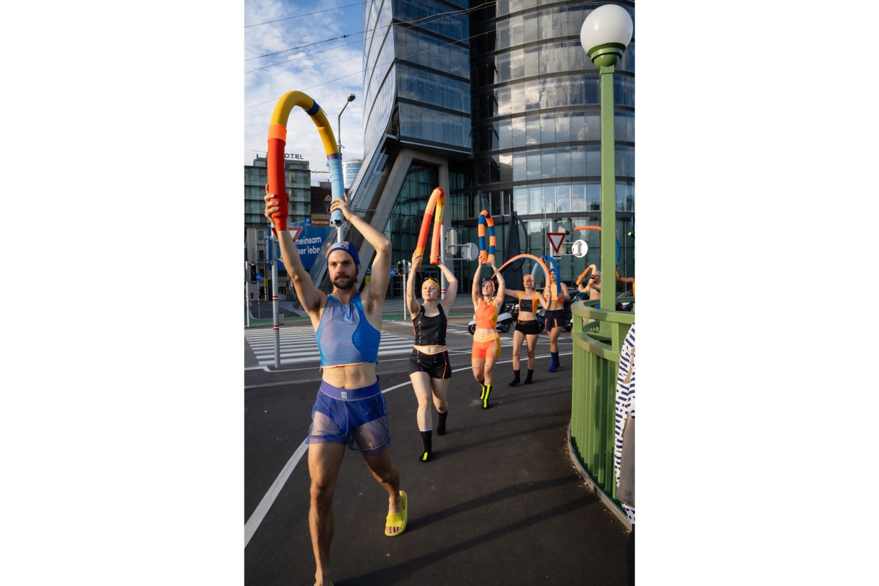 Mehrere Personen in Badekleidung marschieren in einer Reihe mit Badeassesoires 