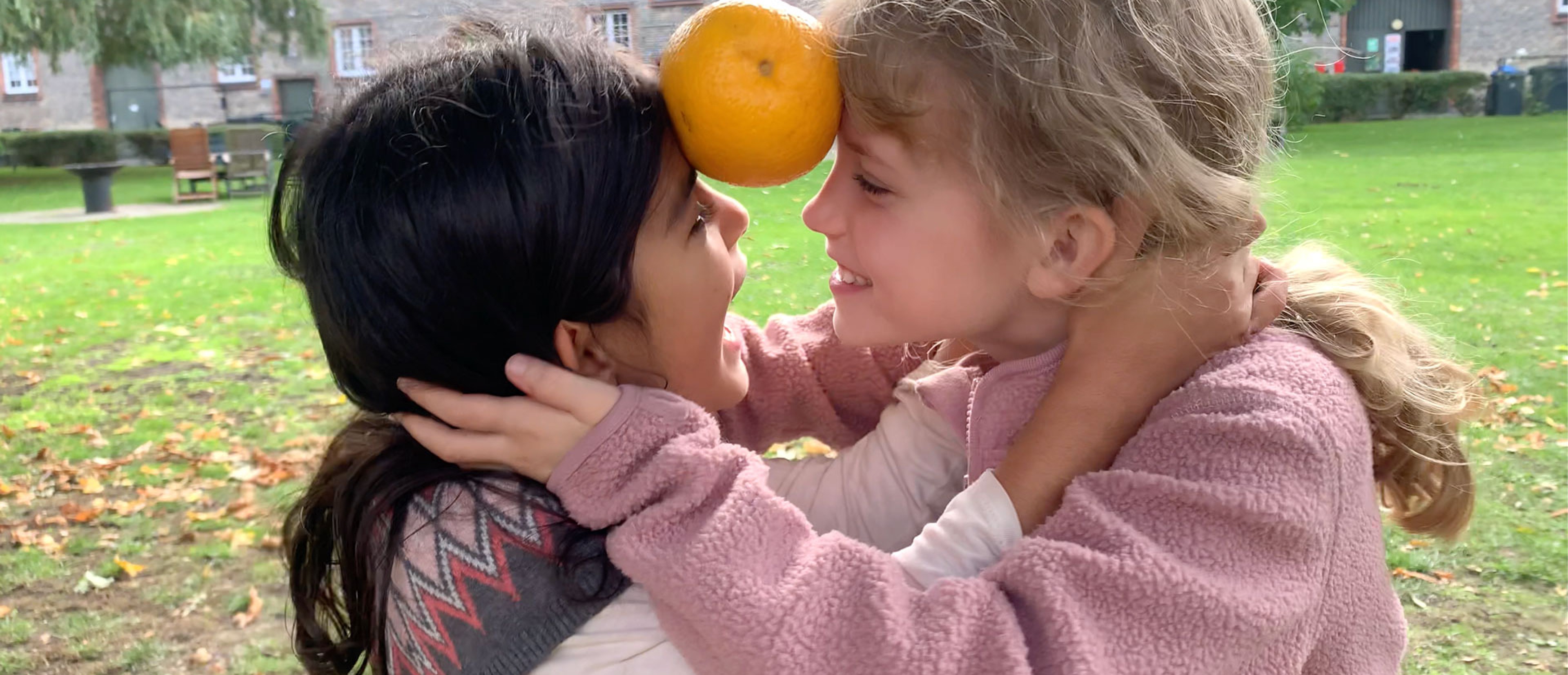 Zwei Mädchen spielen mit einer Orange zwischen der Stirn