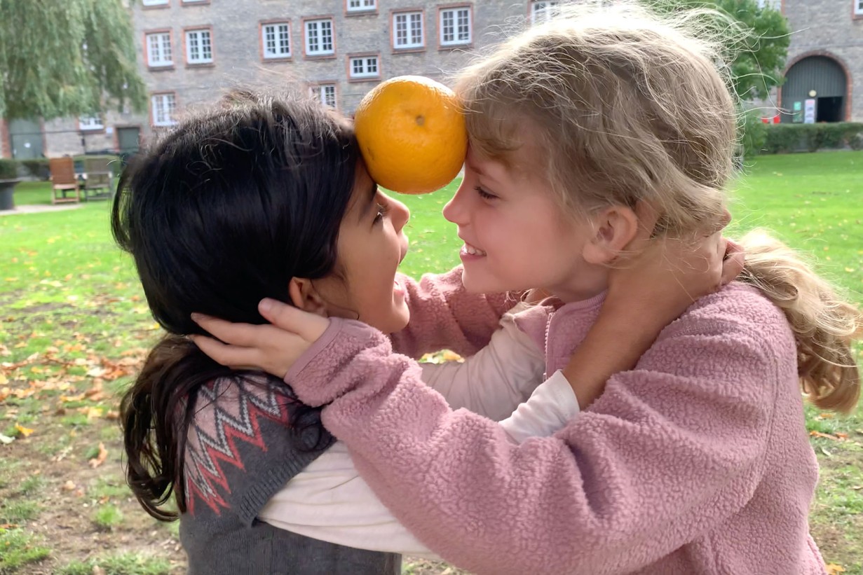 Zwei Mädchen spielen mit einer Orange zwischen der Stirn
