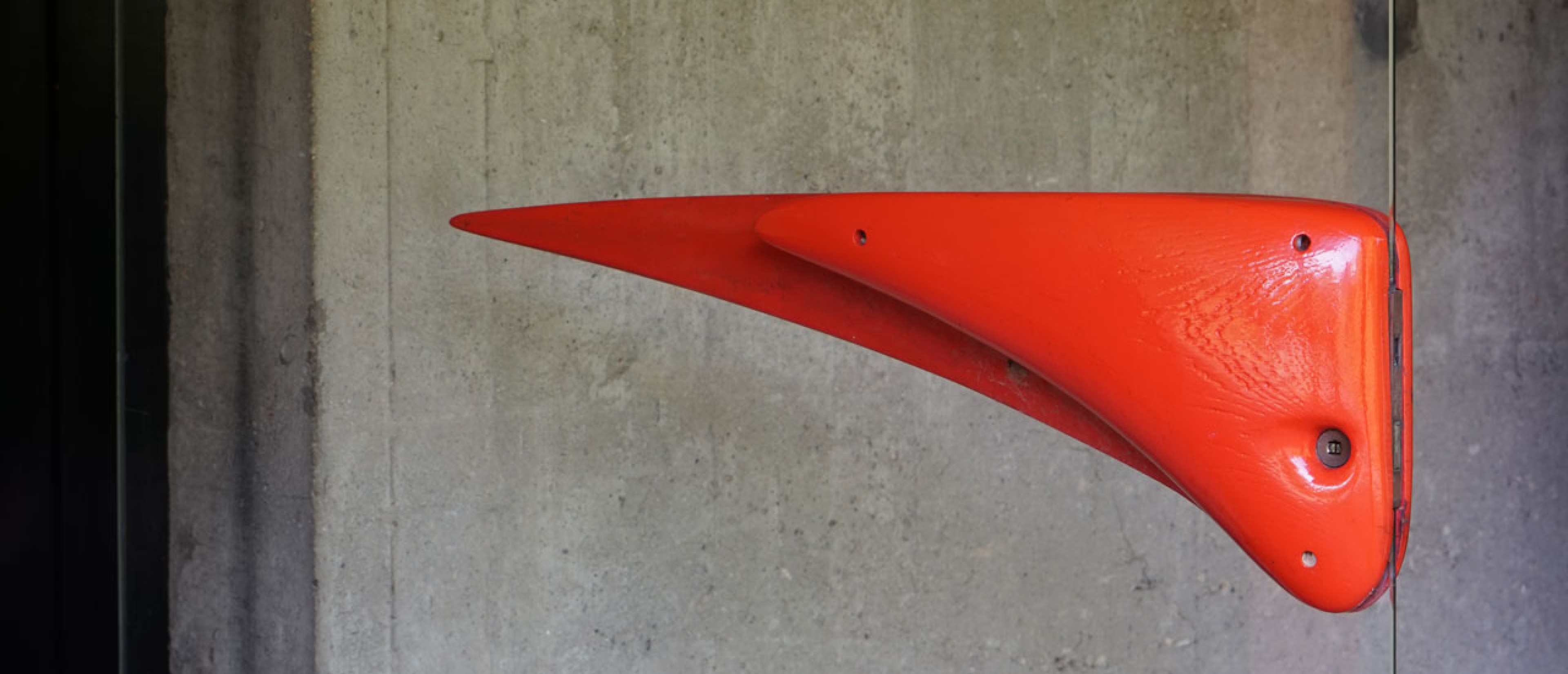 A curved door handle in red on a glass door.