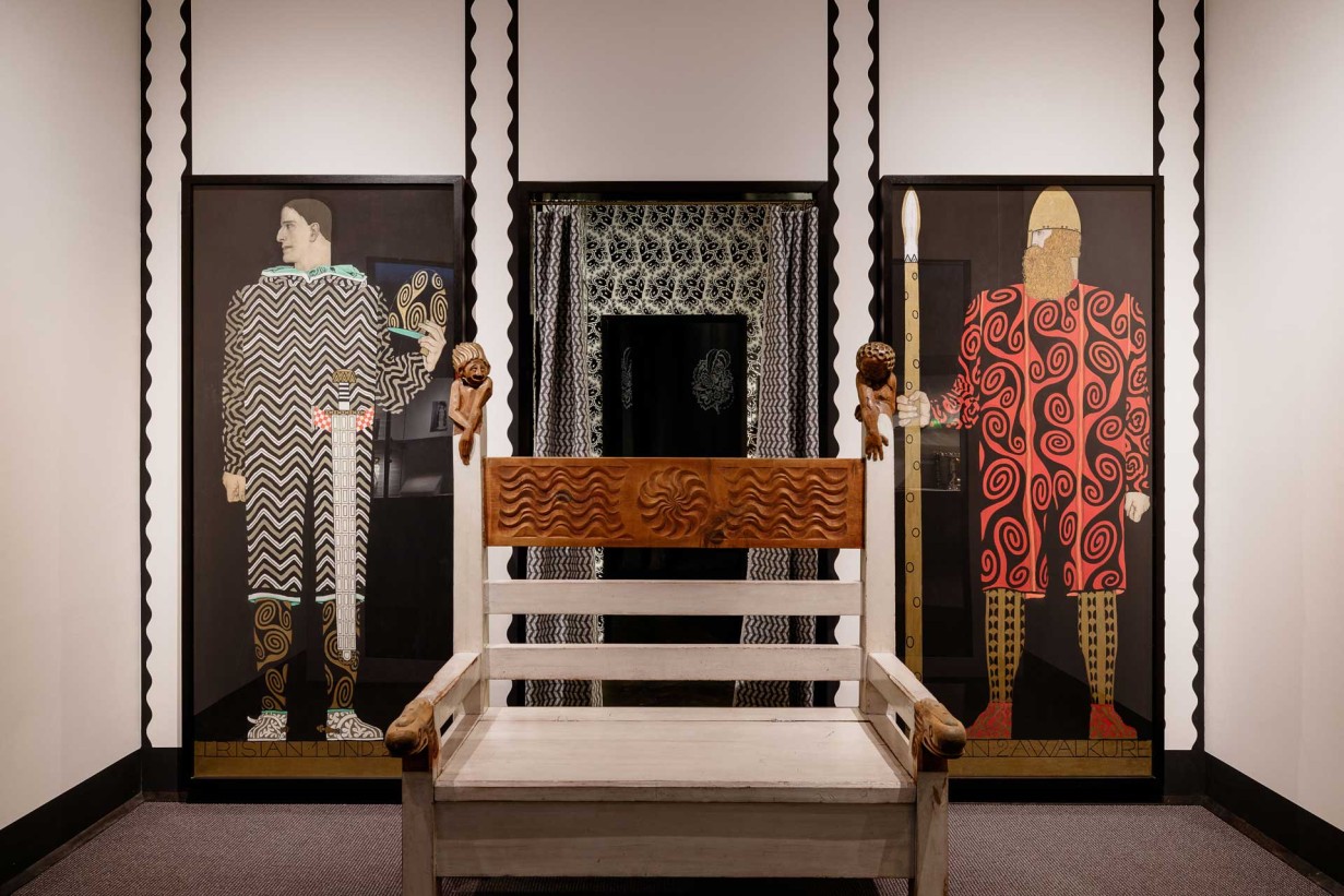 Bank mit kuntsvollen Schnitzereien, im Hintergrund Kostümskizzen für Richard Wagner Oper