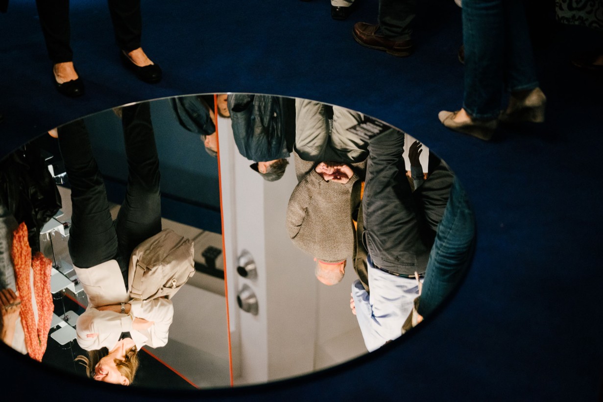 Mirror photographed from above, exhibition visitors are reflected in it.