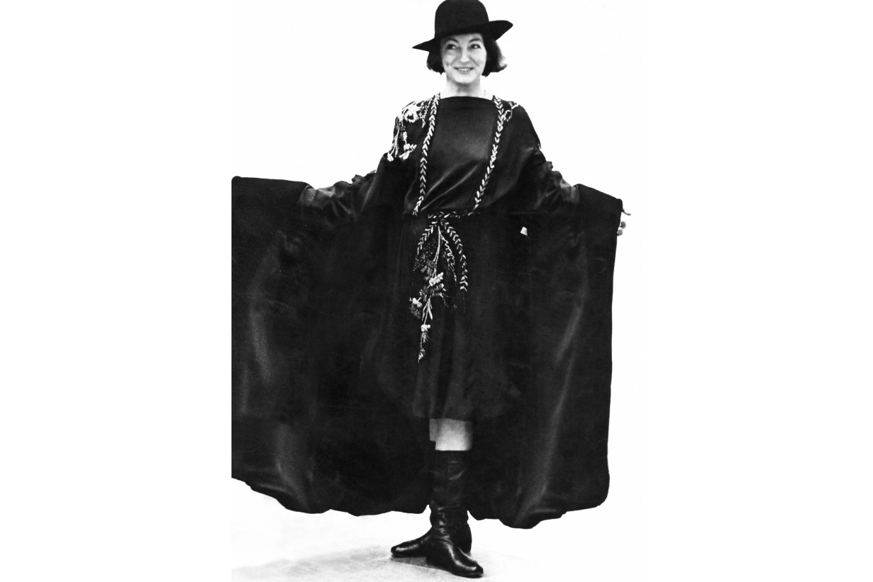 Black and white photograph: It shows a white woman dressed in a black cape, laughing and wearing a hat.
