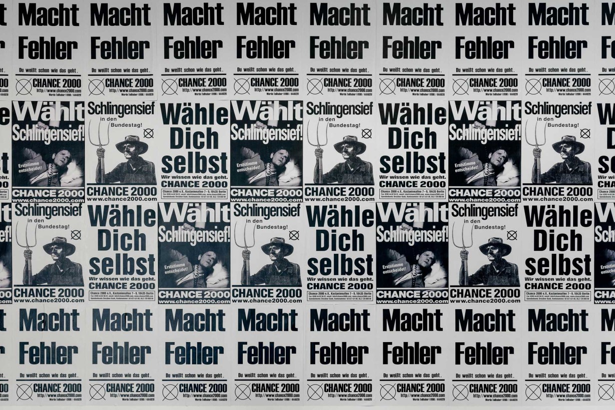 Plakatwand mit Slogans "Macht Fehler", "Wähle dich selbst", Wählt Schlingensief"