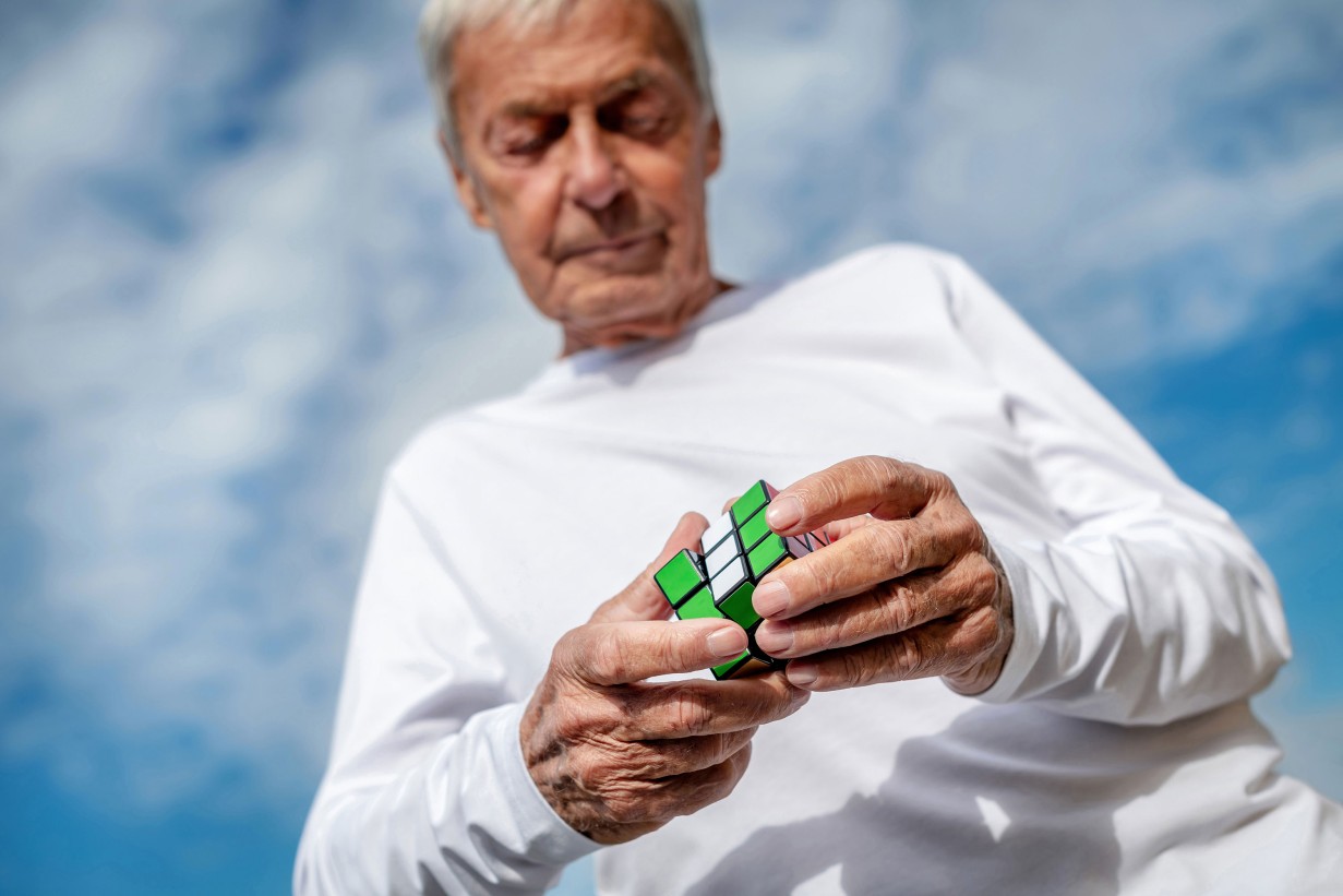 A man holds a Rubik Cube in his hand and looks at it intently. 