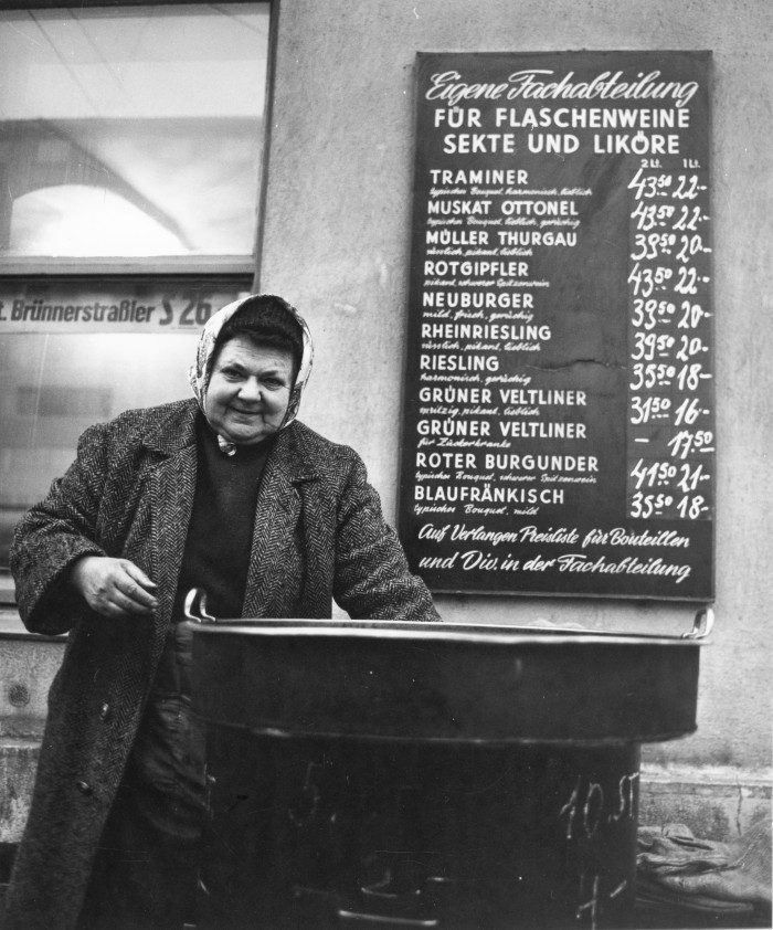 Lächelnde Frau verkauft etwas auf der Straße, hinter ih ein Preisschild für Wein