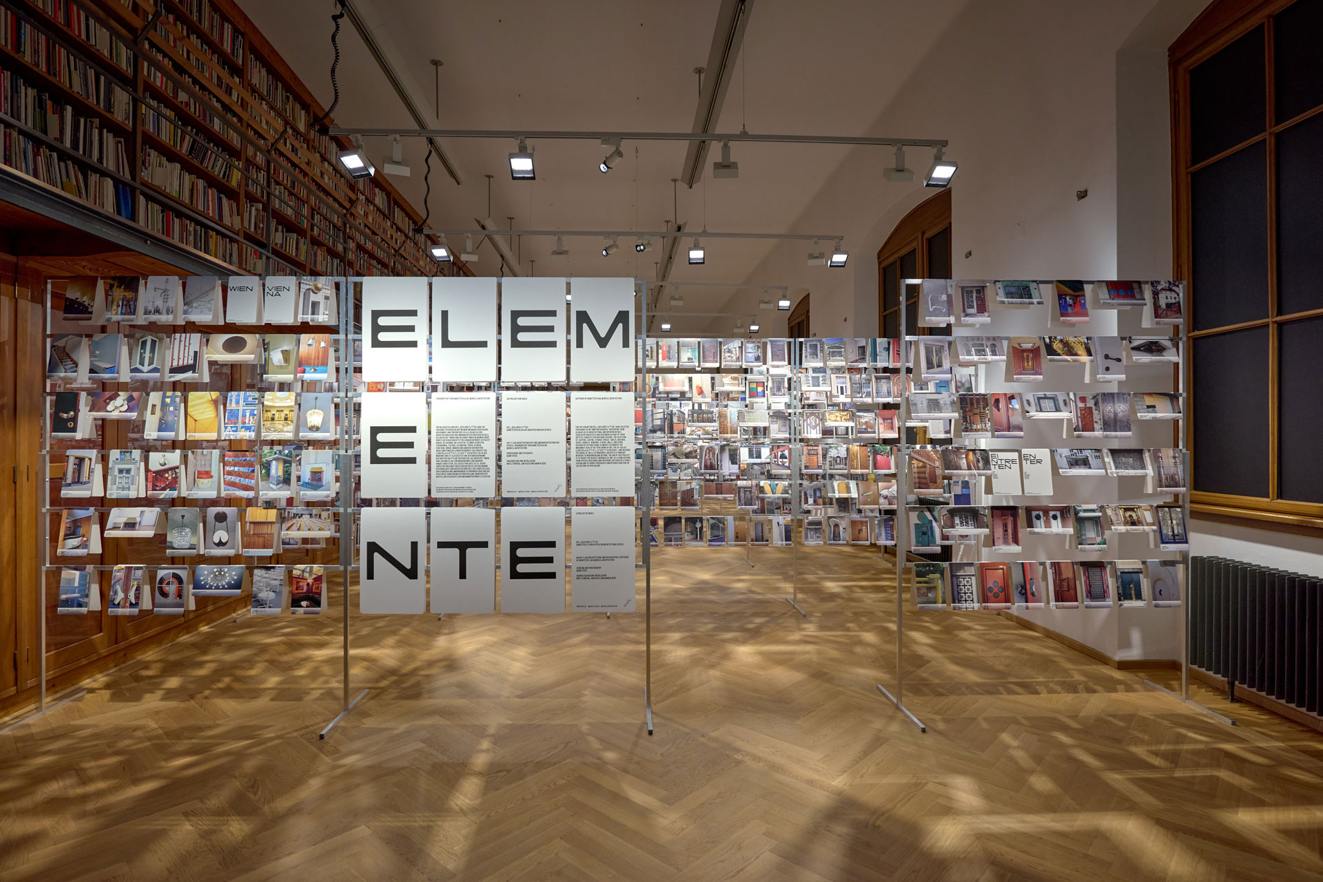 Many photos with detailed shots of architecture hang on scaffolding in an exhibition room.